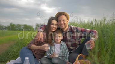 一家人的闲情逸致，微笑的妈妈和爸爸和儿子拥抱，在大自然的绿野野炊中放松